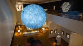 An exhibition space with a lit up moon sculpture hung from the ceiling.